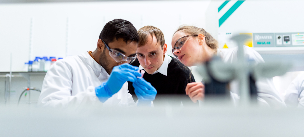 Photographie de 3 personnes examinant un flacon rempli dans un laboratoire