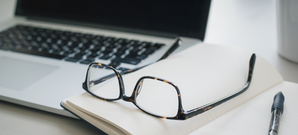 Photographie d'un bureau avec un ordinateur, des lunettes et un stylo