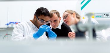 Photographie de 3 personnes examinant un flacon rempli dans un laboratoire