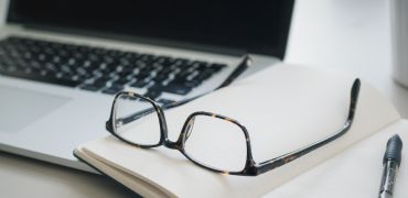 Photographie d'un bureau avec un ordinateur, des lunettes et un stylo