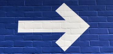Photographie d'une flèche blanche sur un mur bleu